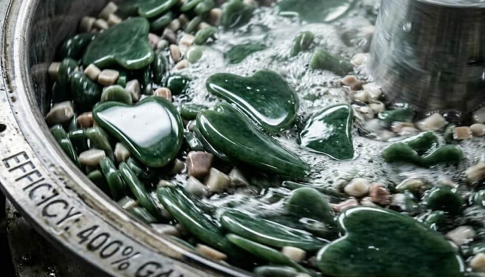 A close-up of jade Gua Sha tools inside a vibratory polishing tumbler.